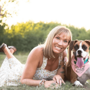 Meaghan Bojarski and her Boxer puppy lay in a field together smiling.